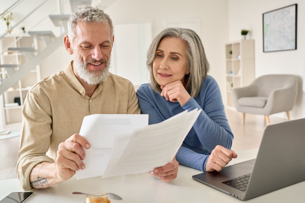 A senior couple sit at a laptop comparing multiple documents